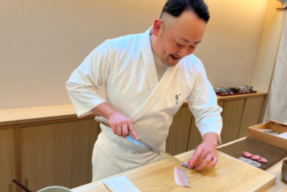 A sushi chef smiling and conversing with guests during a sushi experience at Fukuoka Washoku School